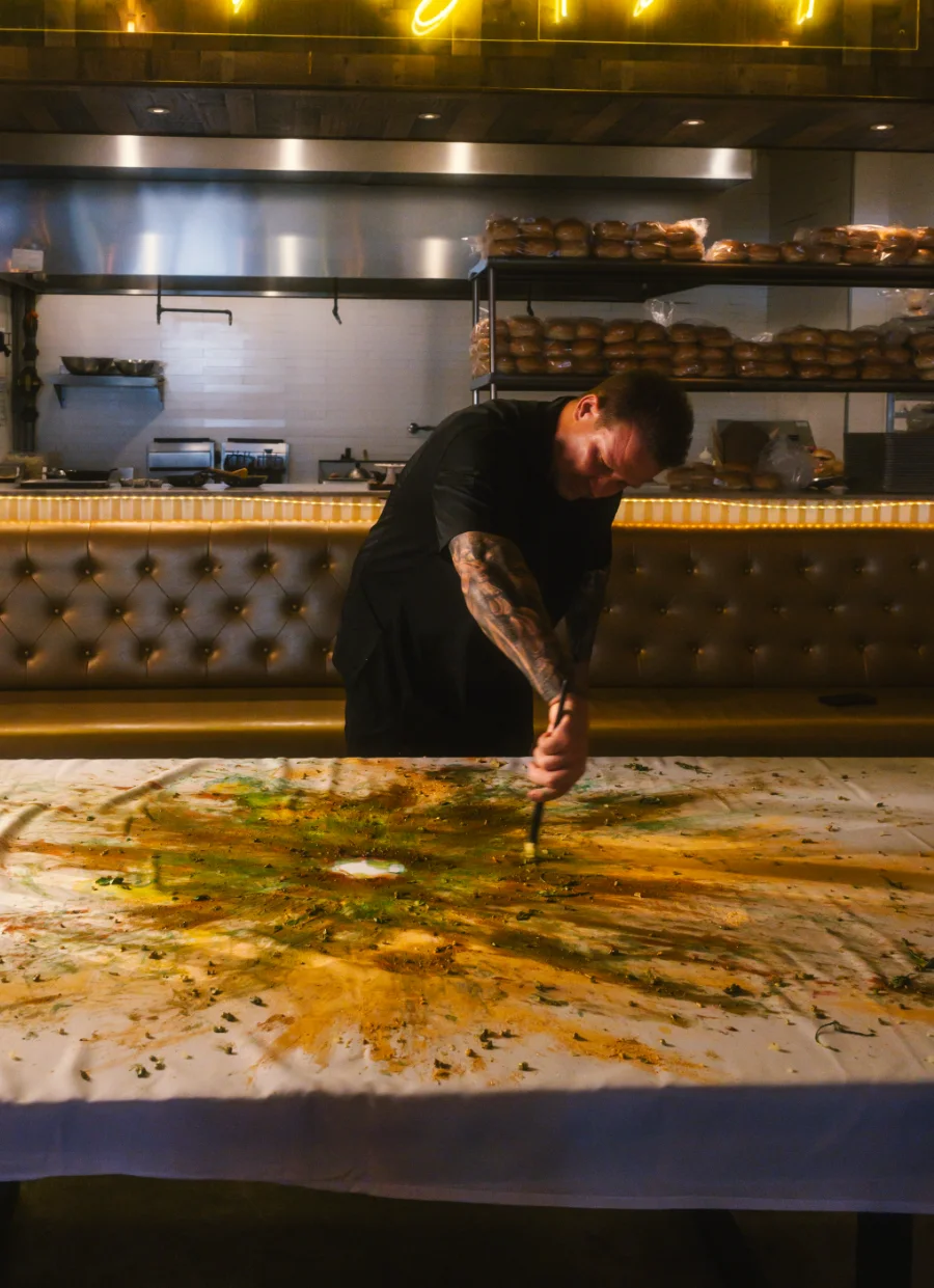 A cook finishing a plated burger on the long table during service